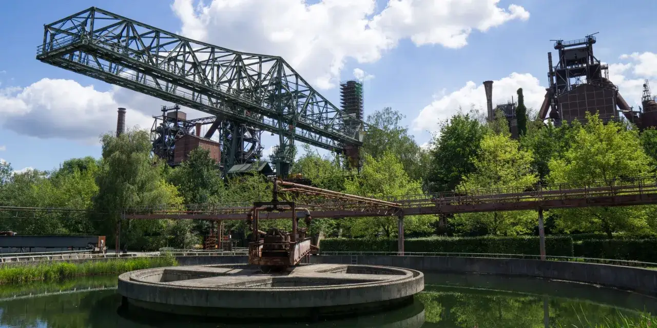 Industriearchitektur trifft Natur im Landschaftspark Duisburg. Ein Kran ragt über einen Teich, umgeben von grünen Bäumen und alten Industrieanlagen.