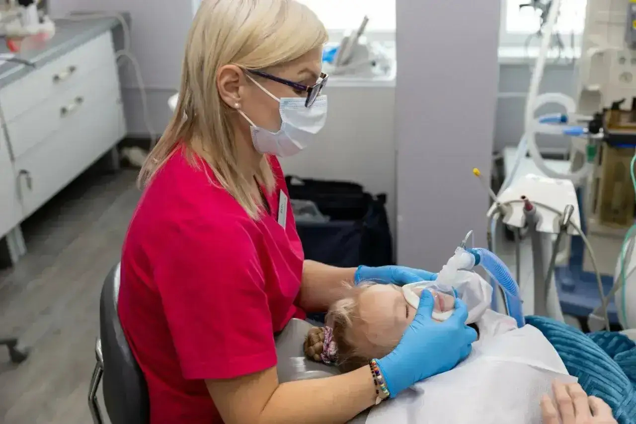 Dentystka w masce i rękawiczkach zakłada dziecku maskę do znieczulenia. Czy znieczulenie u dentysty boli? To pytanie zadaje sobie wielu rodziców.