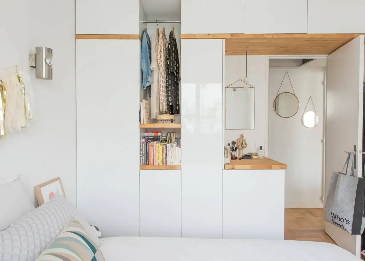 Aménagement astucieux d'une chambre de 11m2 : penderie ouverte, étagères remplies de livres, coin coiffeuse avec miroirs et une grande armoire blanche.