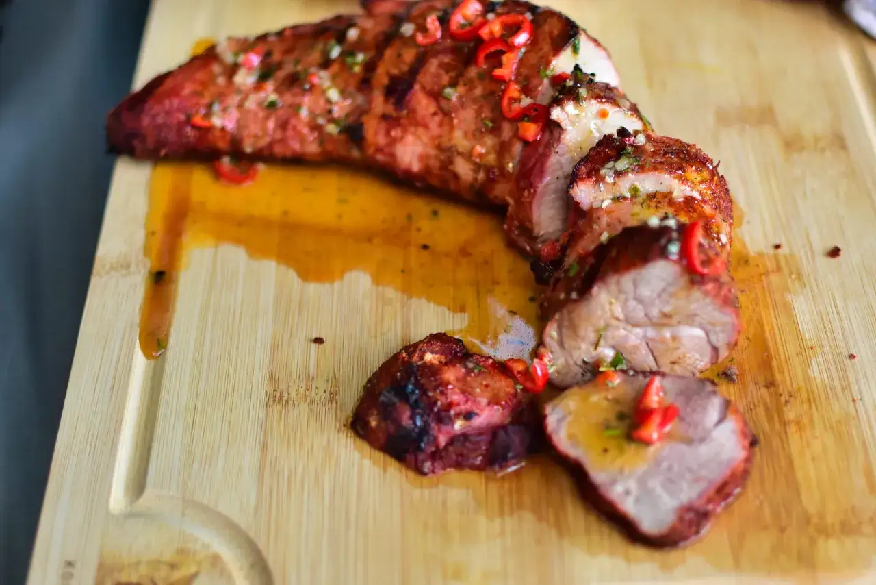 Saftiges schweinefilet grillen, in Scheiben geschnitten, mit Chili und Kräutern garniert, auf einem Holzbrett serviert.