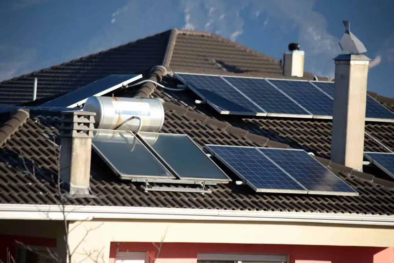 Paneles solares y un acumulador de agua en un tejado, aprovechando la energ&iacute;a solar t&eacute;rmica para un hogar sostenible.
