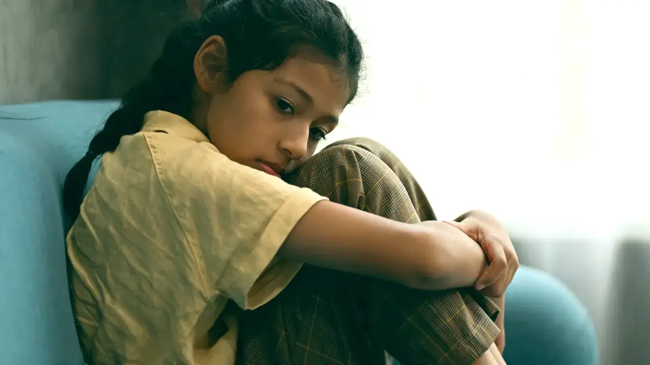Bambina seduta sul divano, con lo sguardo perso nel vuoto. Sembra che mia figlia non abbia amici, e il suo volto esprime tristezza e solitudine.
