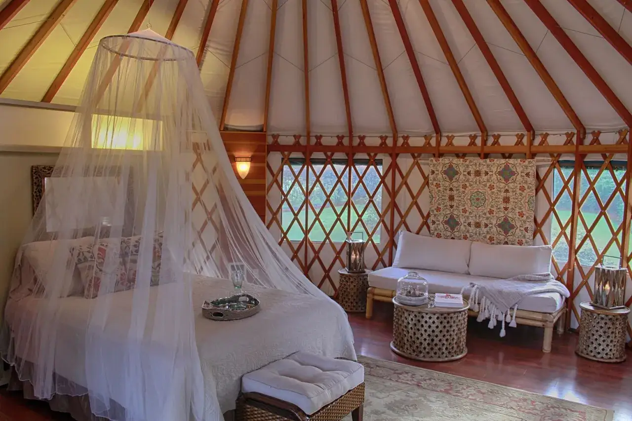 Przytulna glamping jurta z łóżkiem pod baldachimem, sofą i stolikami. Idealne miejsce na relaks.