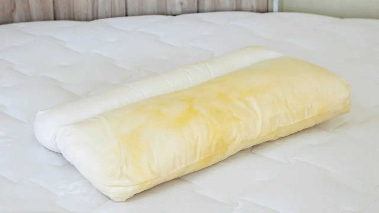A stained pillow on a bed. This is a reminder of how often you should change your pillows on your bed for hygiene.