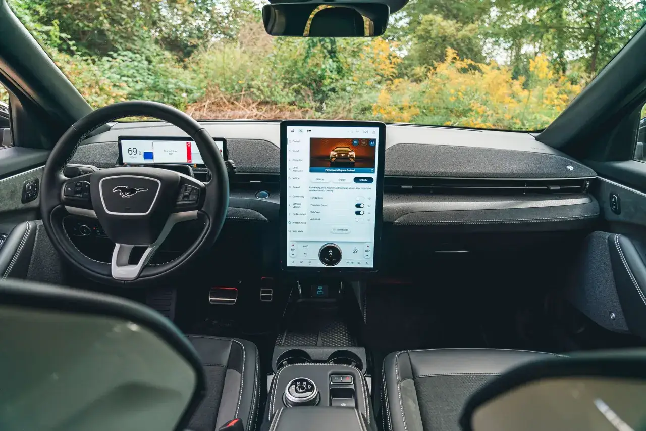 Wnętrze Ford Mustang Mach-E z ekranem multimediów i cyfrowym kokpitem. W tle zieleń drzew.