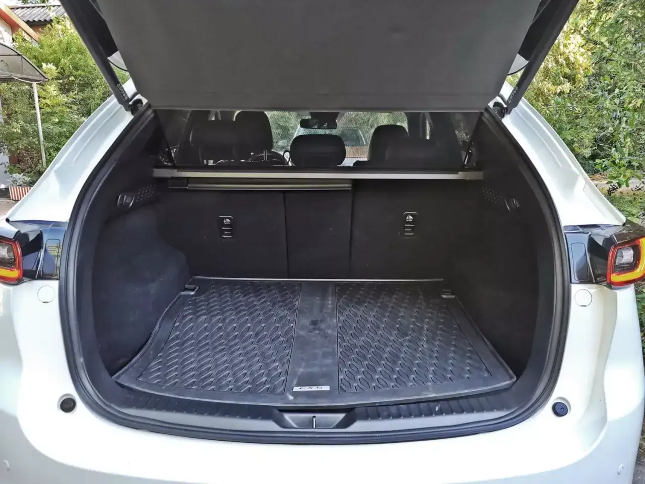 Otwarty bagażnik białej Mazdy CX-5. Widoczny gumowy dywanik i siatka. Wiele pozytywnych mazda cx 5 opinie podkreśla jego przestronność.