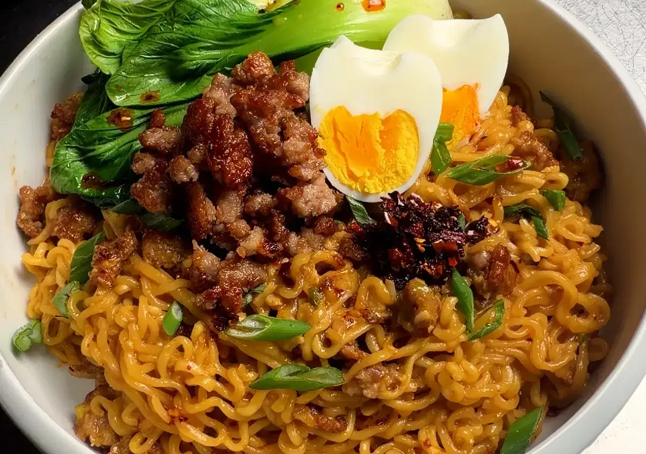 Miseczka pełna tantanmen z mieloną wieprzowiną, jajkiem na twardo, zieloną cebulką i warzywami pak choi.