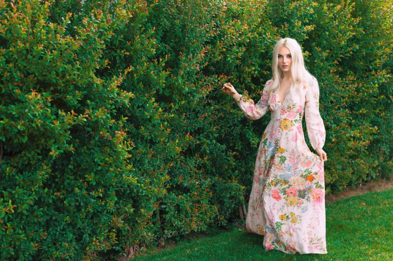 Mujer con vestido floral estilo cottagecore, tocando un seto verde.