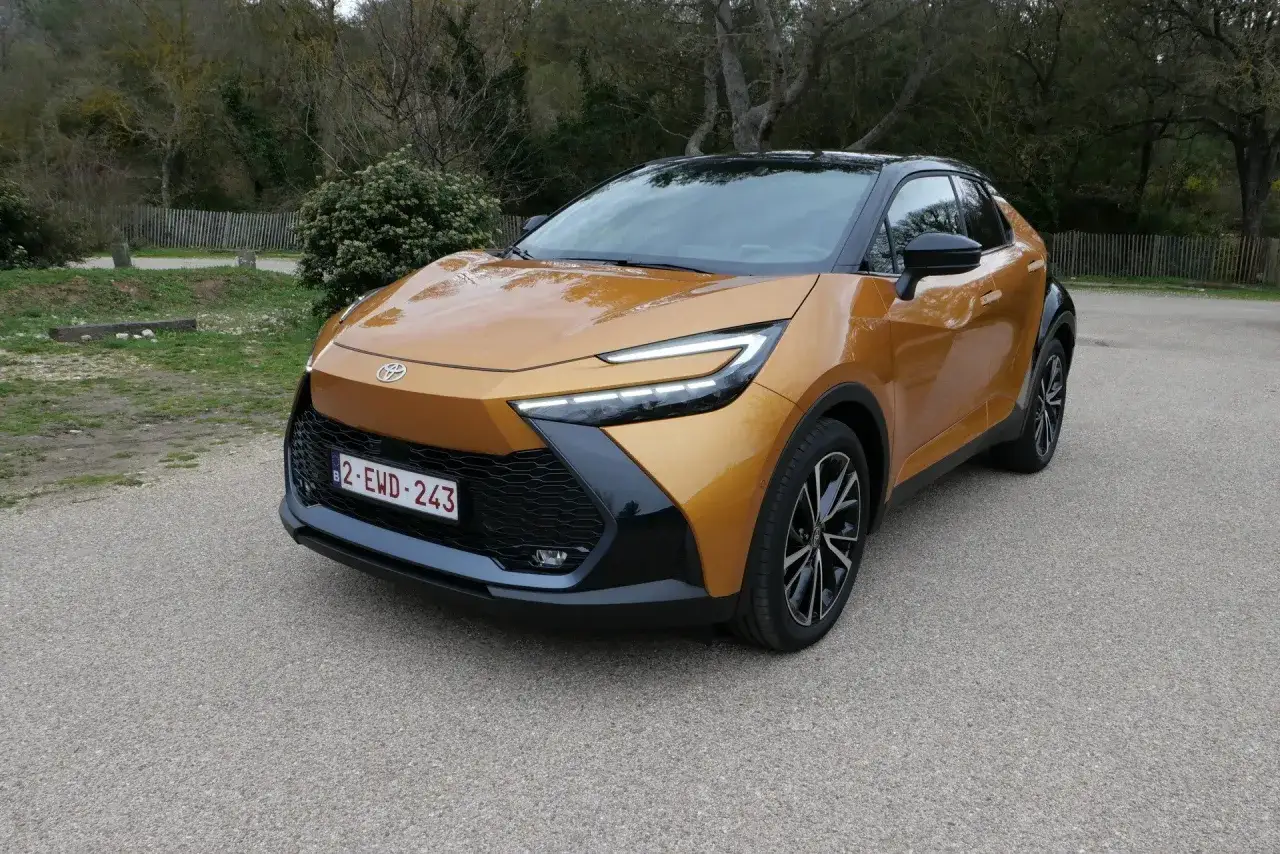 Nowy Toyota C-HR Hybrid w kolorze złocistym, zaparkowany na tle natury.