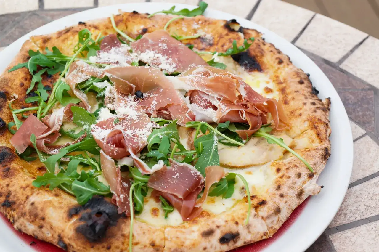En utsökt pizza parma med tunna skivor prosciutto, färsk ruccola och riven parmesanost.