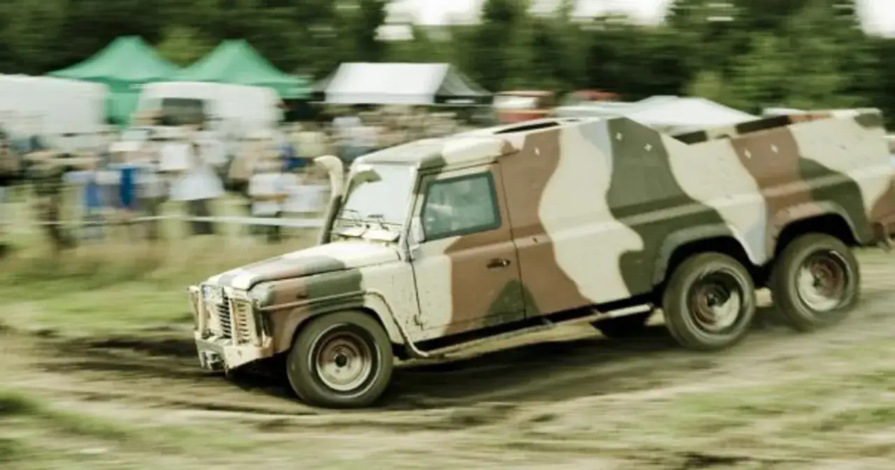 Sześciokołowy pojazd terenowy w kamuflażu, przypominający zmodyfikowanego humvee, przemierza błotnisty teren podczas imprezy off-roadowej.