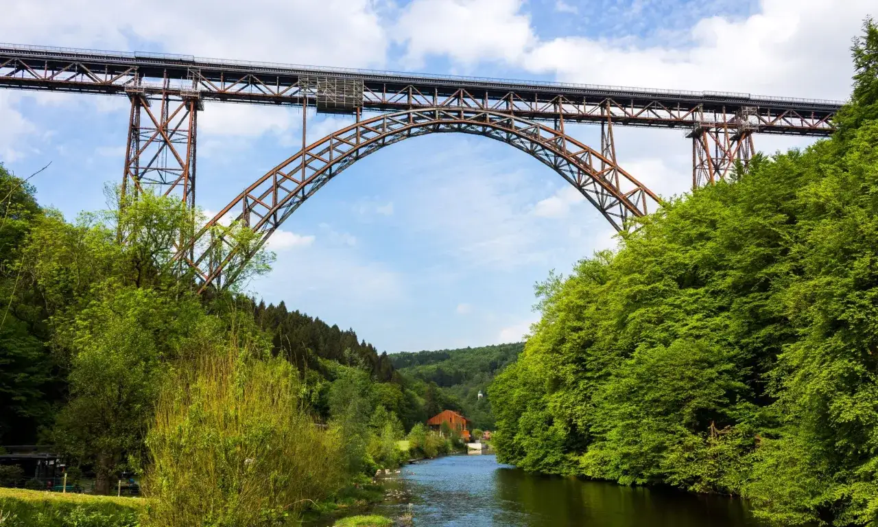 Ein Fluss im Bergischen Land flie&szlig;t unter einer imposanten Eisenbahnbr&uuml;cke hindurch, umgeben von &uuml;ppigem Gr&uuml;n.