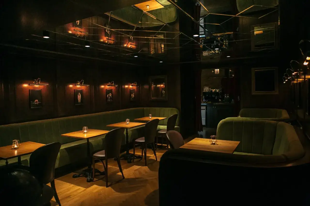 Ambiente íntimo para comer en Budapest. Sofás verdes, mesas de madera y luces cálidas crean un espacio acogedor.