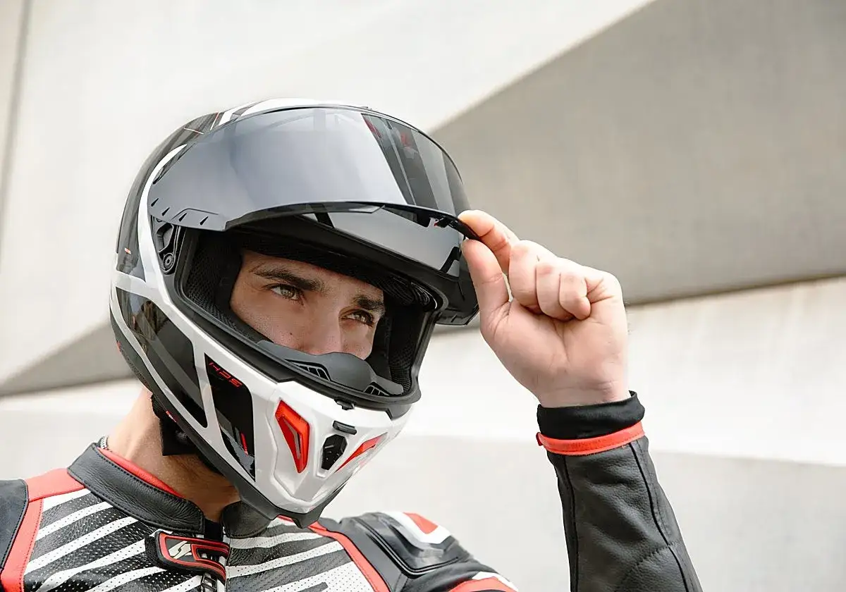 Motorista ajusta su casco, cumpliendo la normativa de cascos moto. Diseño moderno y seguro.