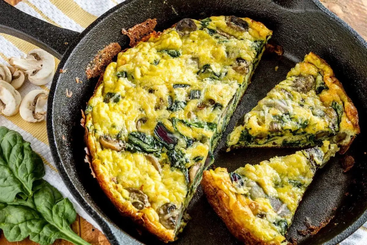 Frittata aux courgettes, &eacute;pinards et champignons, dor&eacute;e et savoureuse, coup&eacute;e en parts dans une po&ecirc;le en fonte.