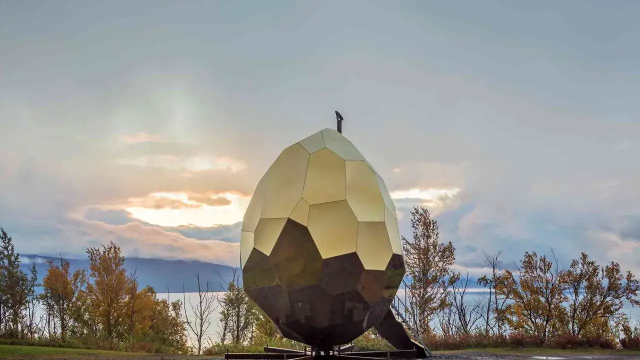 Det gyllene solar egg artipelag, en unik byggnad, står vid en sjö under en molnig himmel.