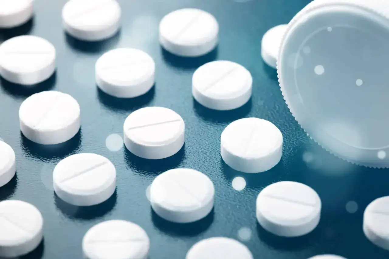 Białe tabletki, niektóre z podziałką, leżą na ciemnym tle. W tle widać białą zakrętkę od opakowania. Mogą to być tabletki ritalin.
