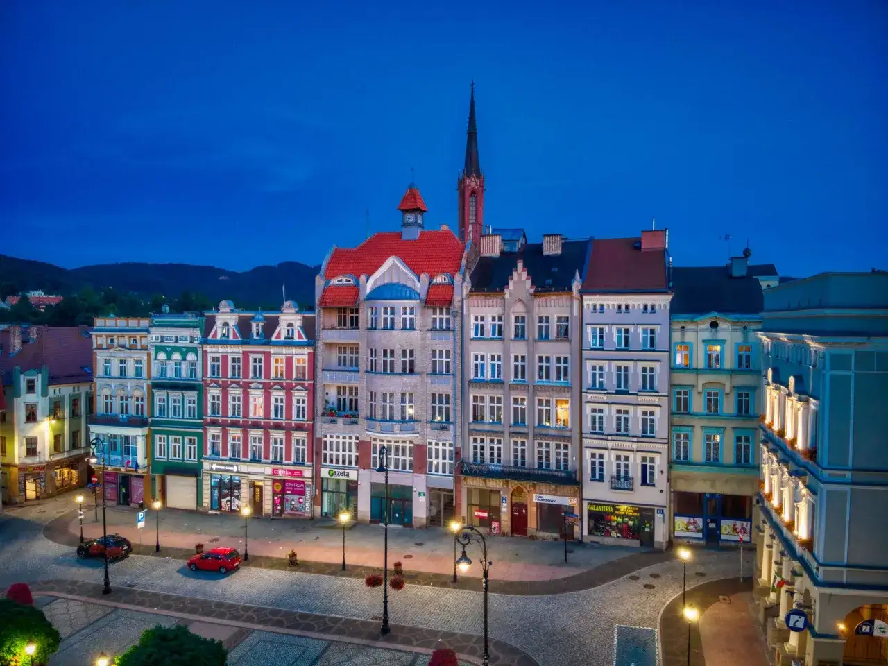 Wieczorny rynek Wałbrzych. Kolorowe kamienice, kościelna wieża i puste ulice oświetlone latarniami.