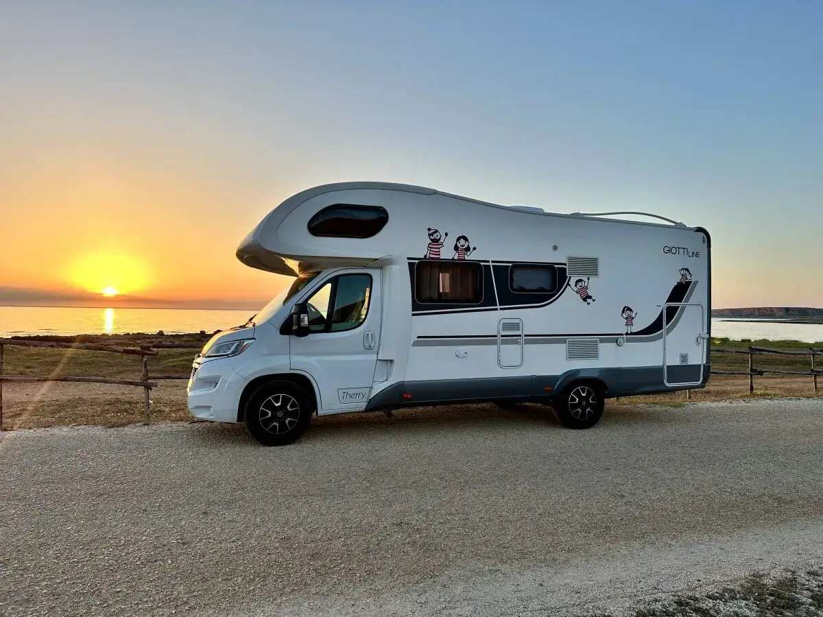 Autocaravana blanca aparcada en la costa, disfrutando de un atardecer espectacular. ¡La aventura de **Sicilia en autocaravana** comienza!