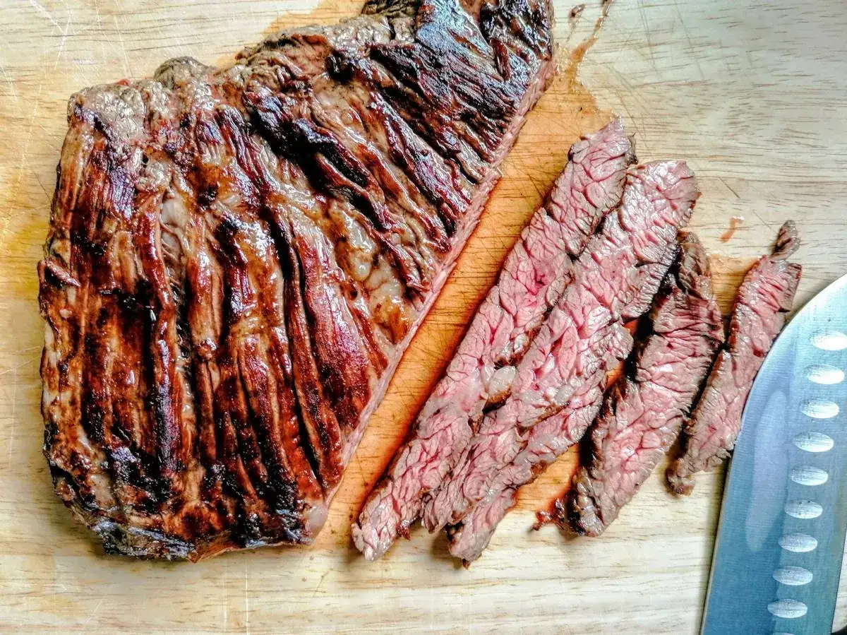 Un succulento diaframma di manzo grigliato, tagliato a fette sottili su un tagliere di legno, pronto per essere gustato.