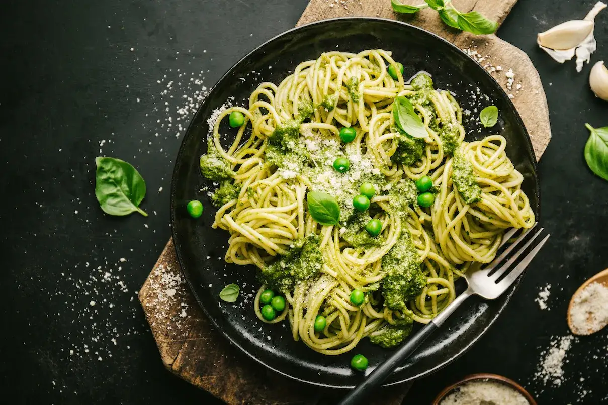 Pyszny makaron z pesto ze słoika, udekorowany groszkiem i listkami bazylii, gotowy do podania.