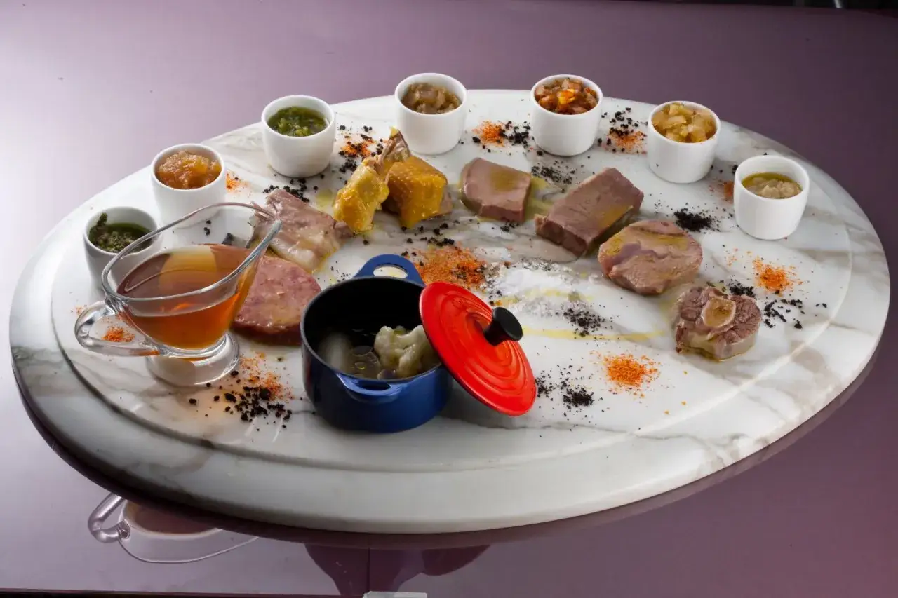 Un ricco bollito di carne, con diverse salse e contorni, presentato su un piatto di marmo.