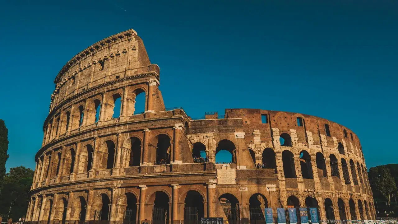 The Colosseum stands majestically under a clear blue sky. Tourists explore its ancient arches, a testament to its enduring appeal. Is Rome safe? This iconic landmark suggests a city full of history and life.