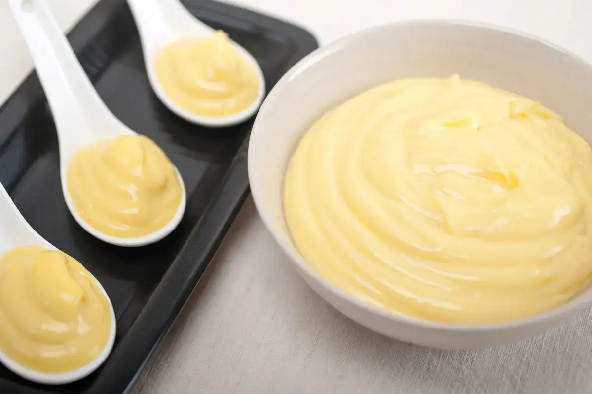 Crema pasticcera senza latte, liscia e vellutata, servita in cucchiai e una ciotola. Perfetta per chi cerca un'alternativa leggera.