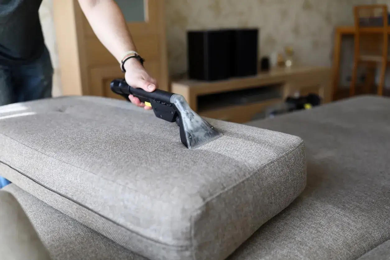 Main tenant utilise un appareil pour nettoyer canapé tissu vapeur. La vapeur pénètre les fibres pour un nettoyage en profondeur.