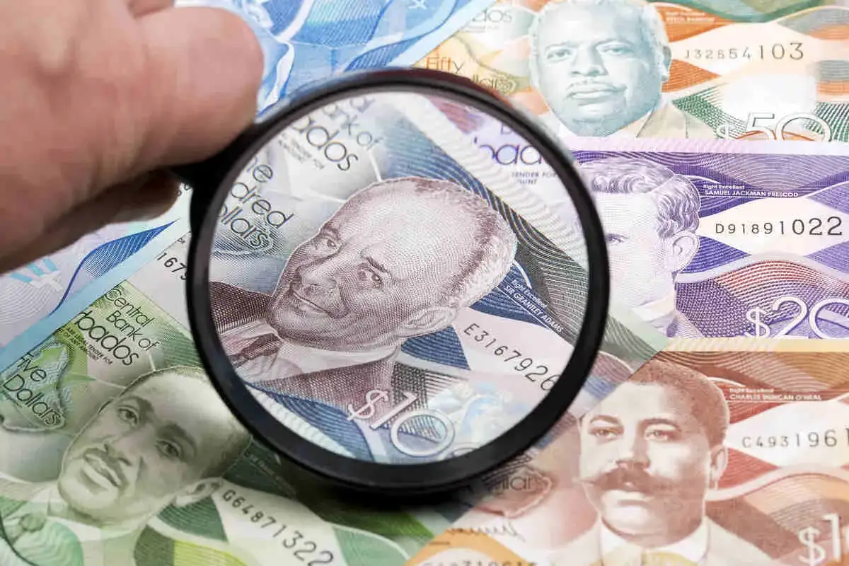 Förstoringsglas granskar sedlar med porträtt, visar Barbados valuta.