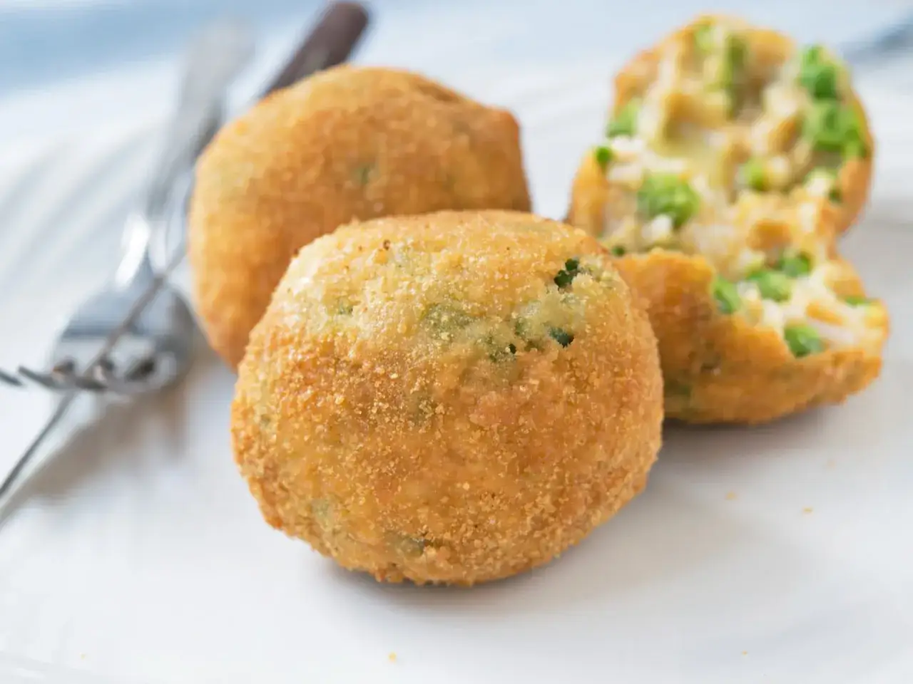 Drei goldbraune, knusprige Arancini, gef&uuml;llt mit Reis und Erbsen, liegen auf einem Teller.