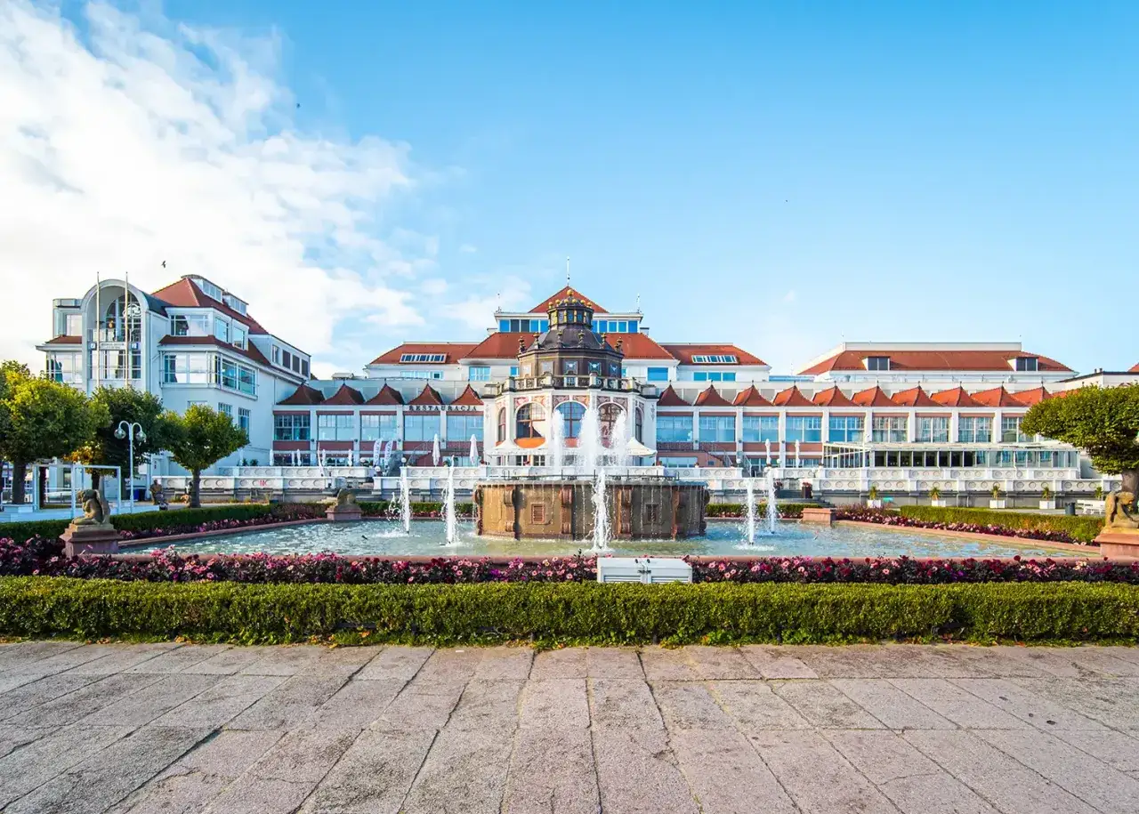 Sopot architektura: fontanna przed budynkiem z czerwonym dachem i białymi ścianami, ozdobiona detalami.