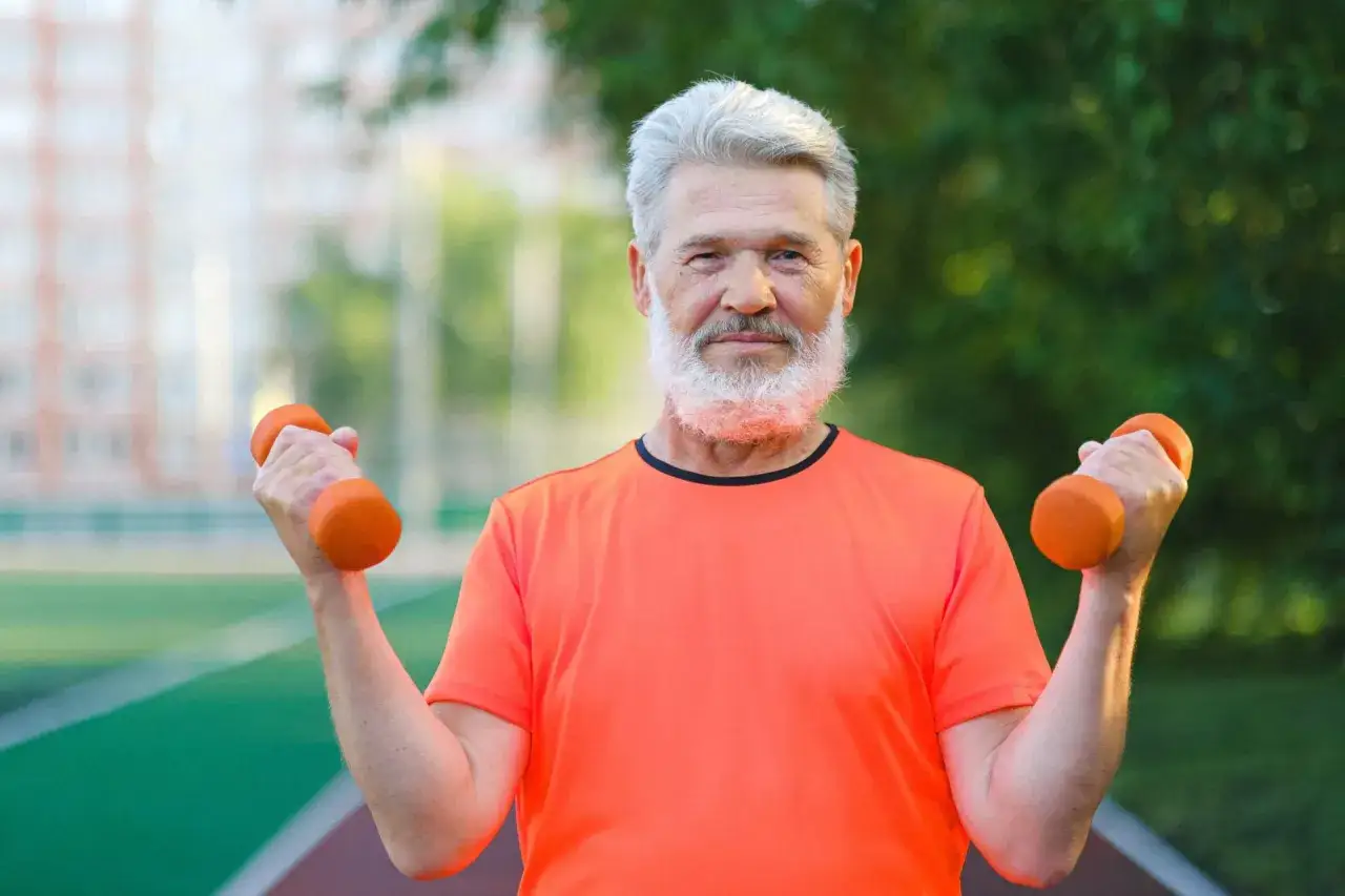 Ein Mann mit grauem Bart und Haar trainiert mit Hanteln. Muskelaufbau mit 70 Jahren ist möglich!