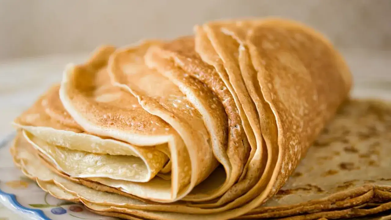 Pile de crêpes dorées, prêtes pour le temps de repos de la pâte à crêpe. Elles sont empilées sur une assiette décorée.