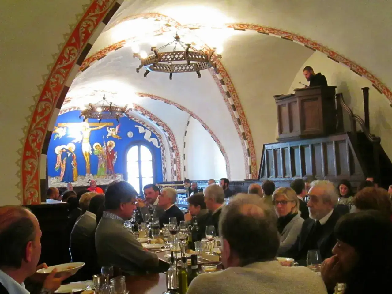 A formal dinner is underway in a monastery dining hall, with a monk speaking from a pulpit. This gathering offers a glimpse into what monks eat during communal meals.