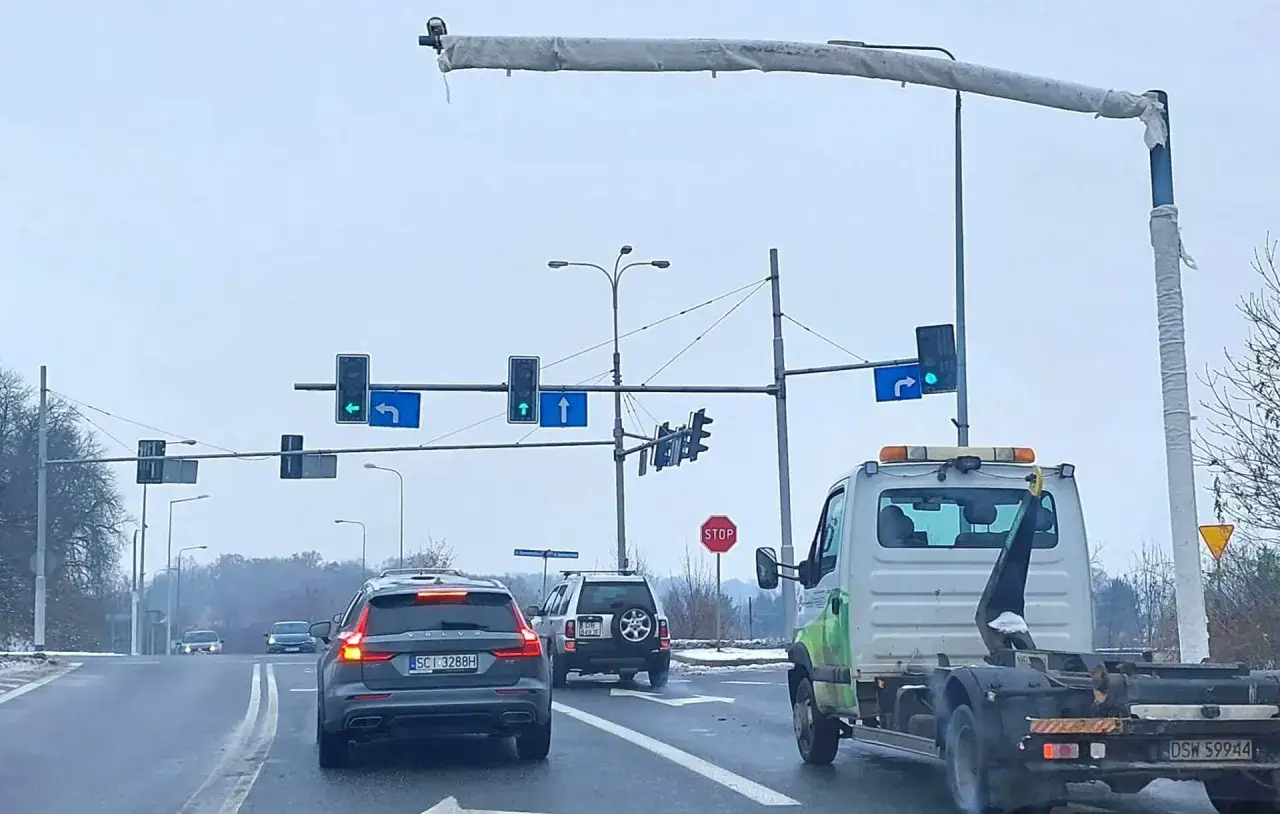 Na skrzyżowaniu, gdzie zielone światła kierują ruchem, kamery rejestrują co się dzieje. Widać samochody, ciężarówkę i znaki drogowe.