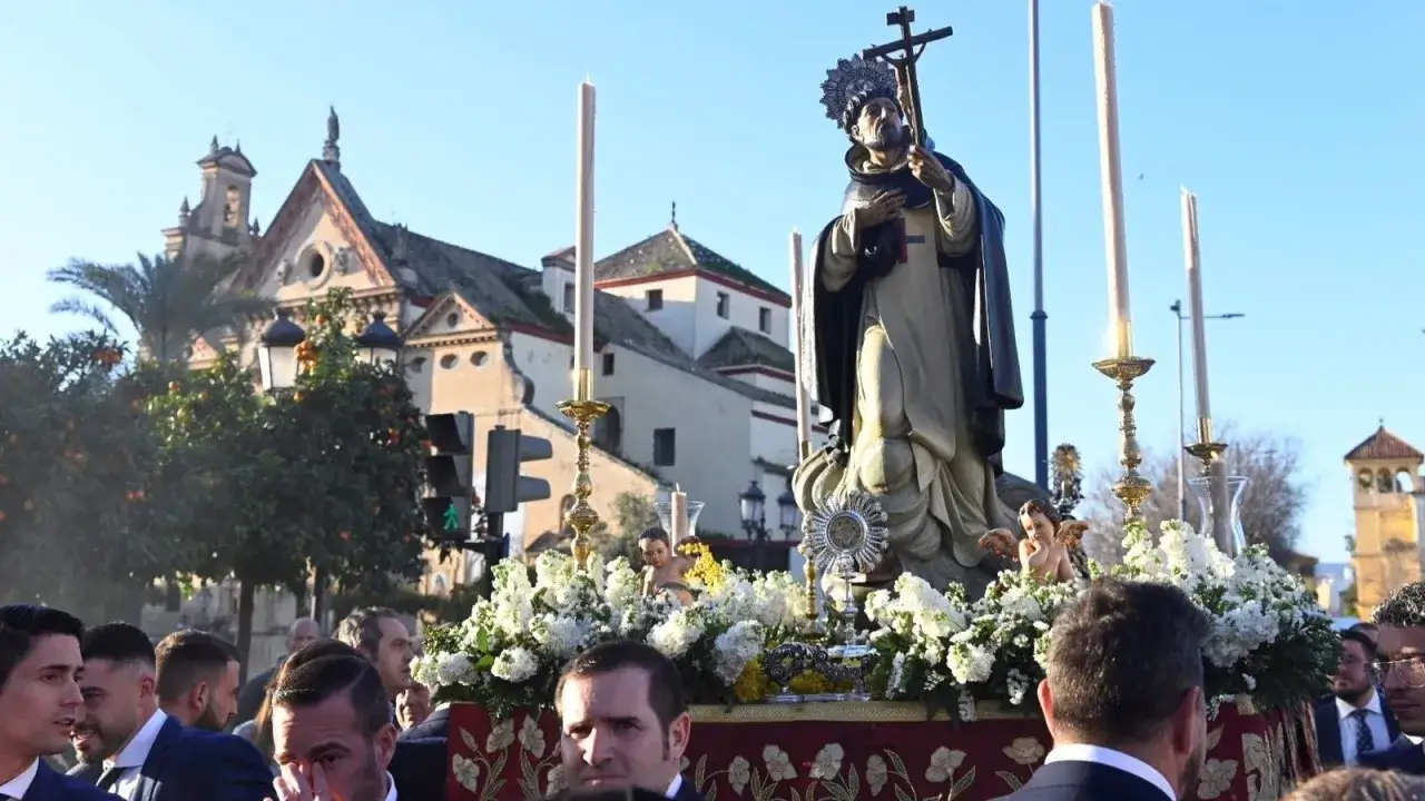 Procesión de San Juan Bautista de la Concepción, con la imagen del santo sobre un paso adornado con flores y velas, ante una iglesia.