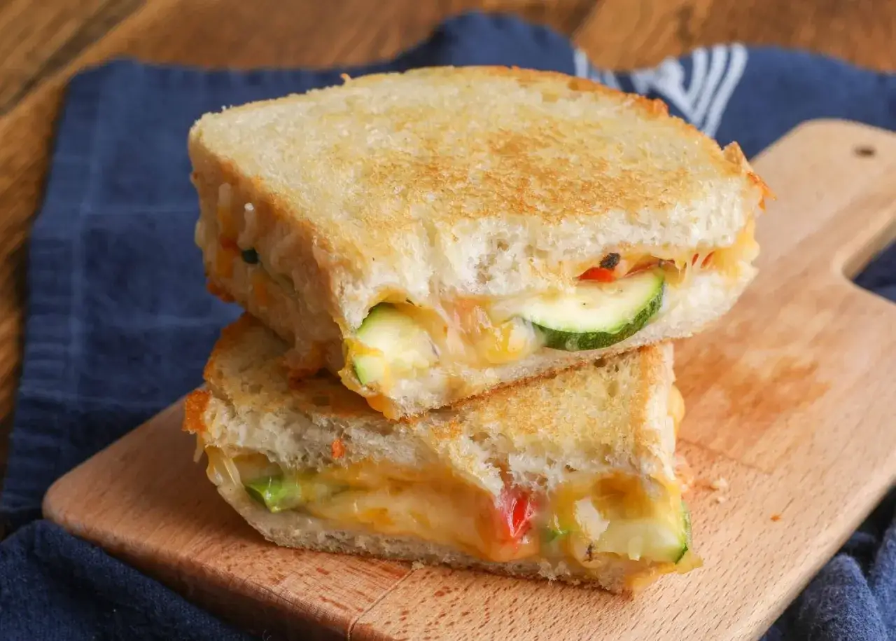 Zwei goldbraune gegrillte Sandwiches mit geschmolzenem K&auml;se und Zucchinischeiben, inspiriert von leckeren Sandwichmaker Rezepten.