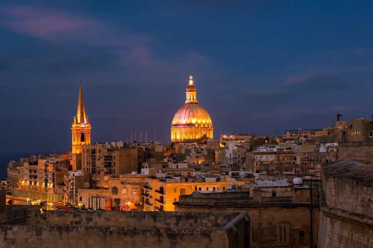 Malta co zobaczyć: Valletta nocą, z oświetloną kopułą i wieżą kościelną, tworzy magiczny widok.