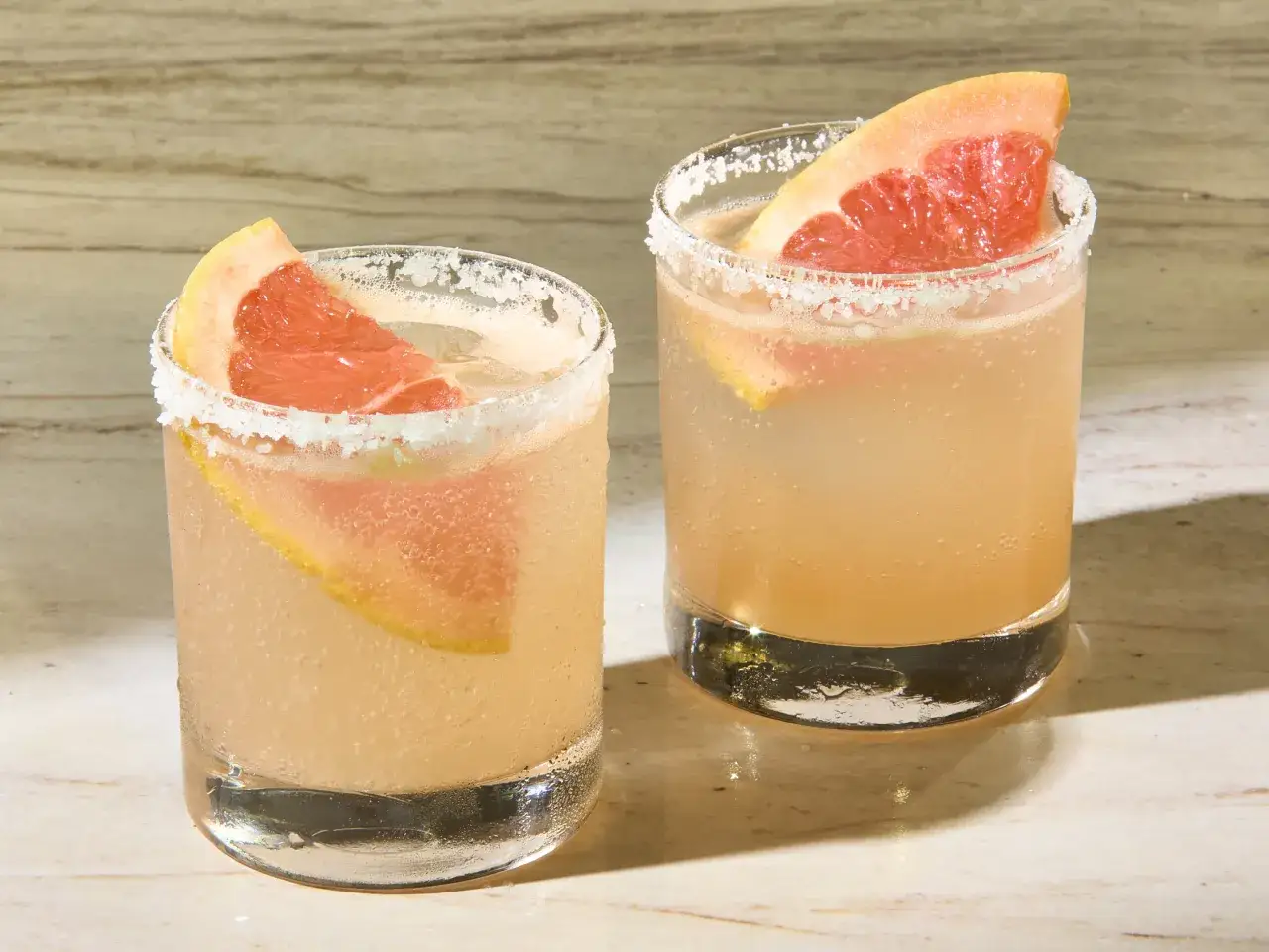 Två glas med en uppfriskande paloma drink, garnerade med grapefruktklyftor och saltkant.