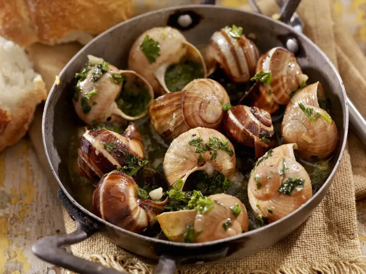 Pyszne escargot, czyli ślimaki w skorupkach z ziołami i czosnkiem, podane w metalowej patelni.