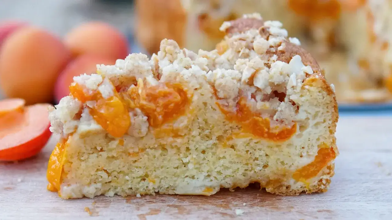 Una fetta di torta alle albicocche cremosa, con albicocche succose e una crosta croccante, pronta per essere gustata.