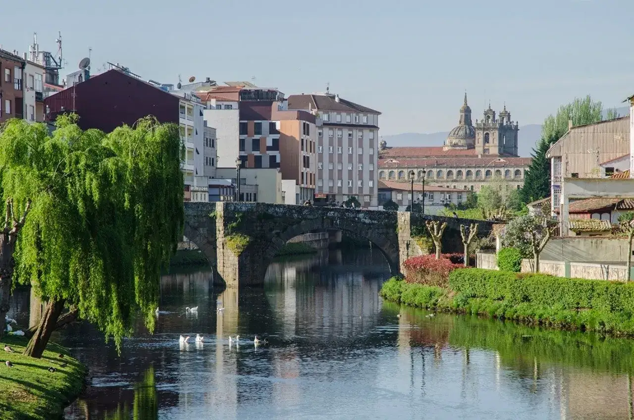 Un r&iacute;o tranquilo atraviesa un pueblo con un puente de piedra y edificios hist&oacute;ricos. Un lugar encantador, como otros pueblos bonitos cerca de Monforte de Lemos.