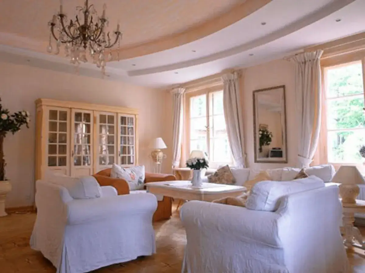 Gem&uuml;tliches Wohnzimmer im mediterranen Landhausstil mit wei&szlig;en Sofas, einem Vitrinenschrank und Kronleuchter.