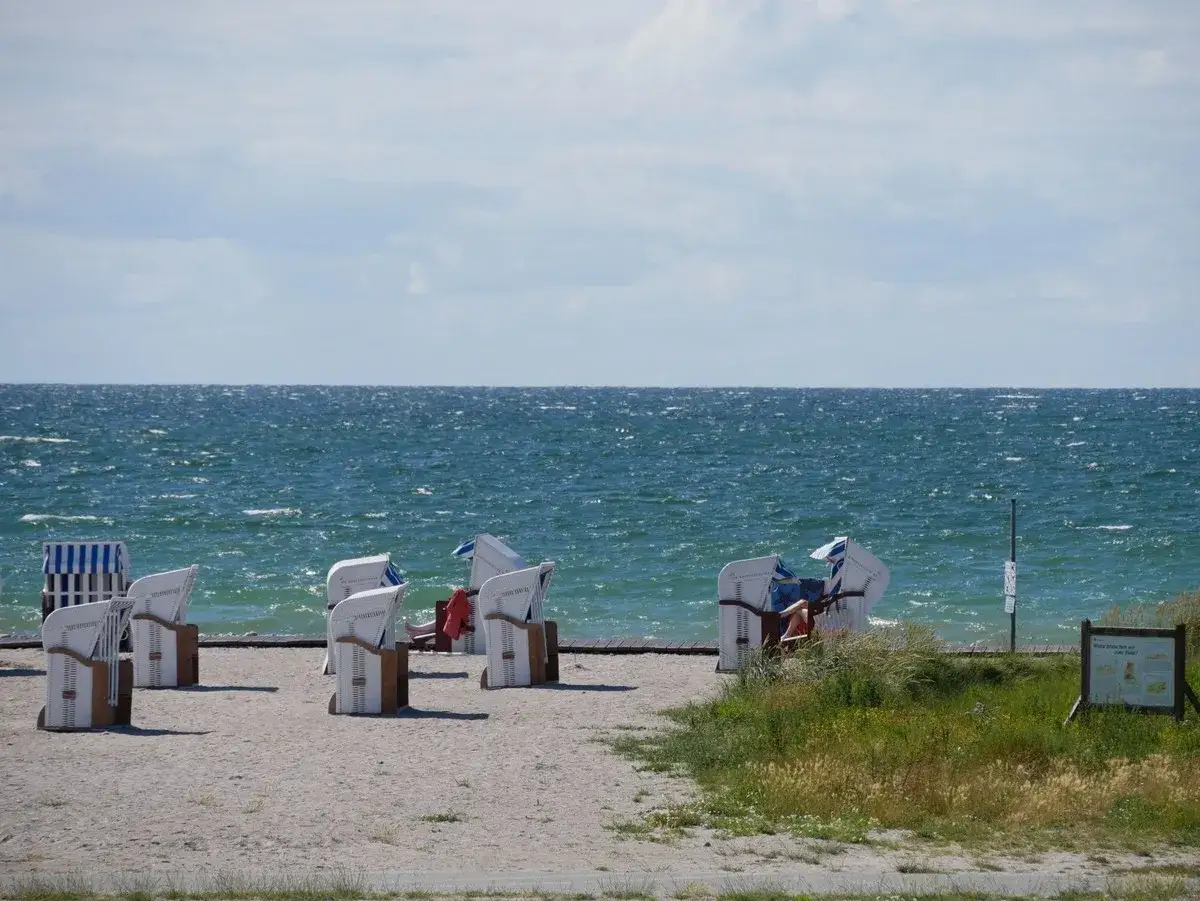 Leere und besetzte Strandkörbe am **Bojendorfer Strand** laden zum Entspannen ein. Das Meer glitzert, Wolken ziehen vorbei.