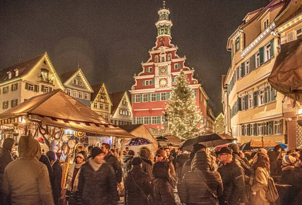Ein belebter Weihnachtsmarkt in Deutschland, ein echter Geheimtipp! Menschen schlendern zwischen Ständen unter einem festlich geschmückten Baum.