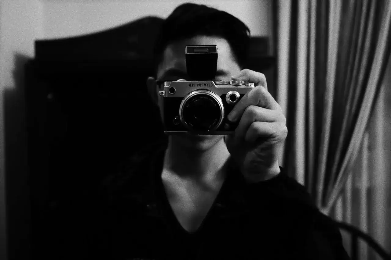 A person holds an Olympus PEN F camera, showcasing its classic design and interchangeable Olympus PEN F lenses.