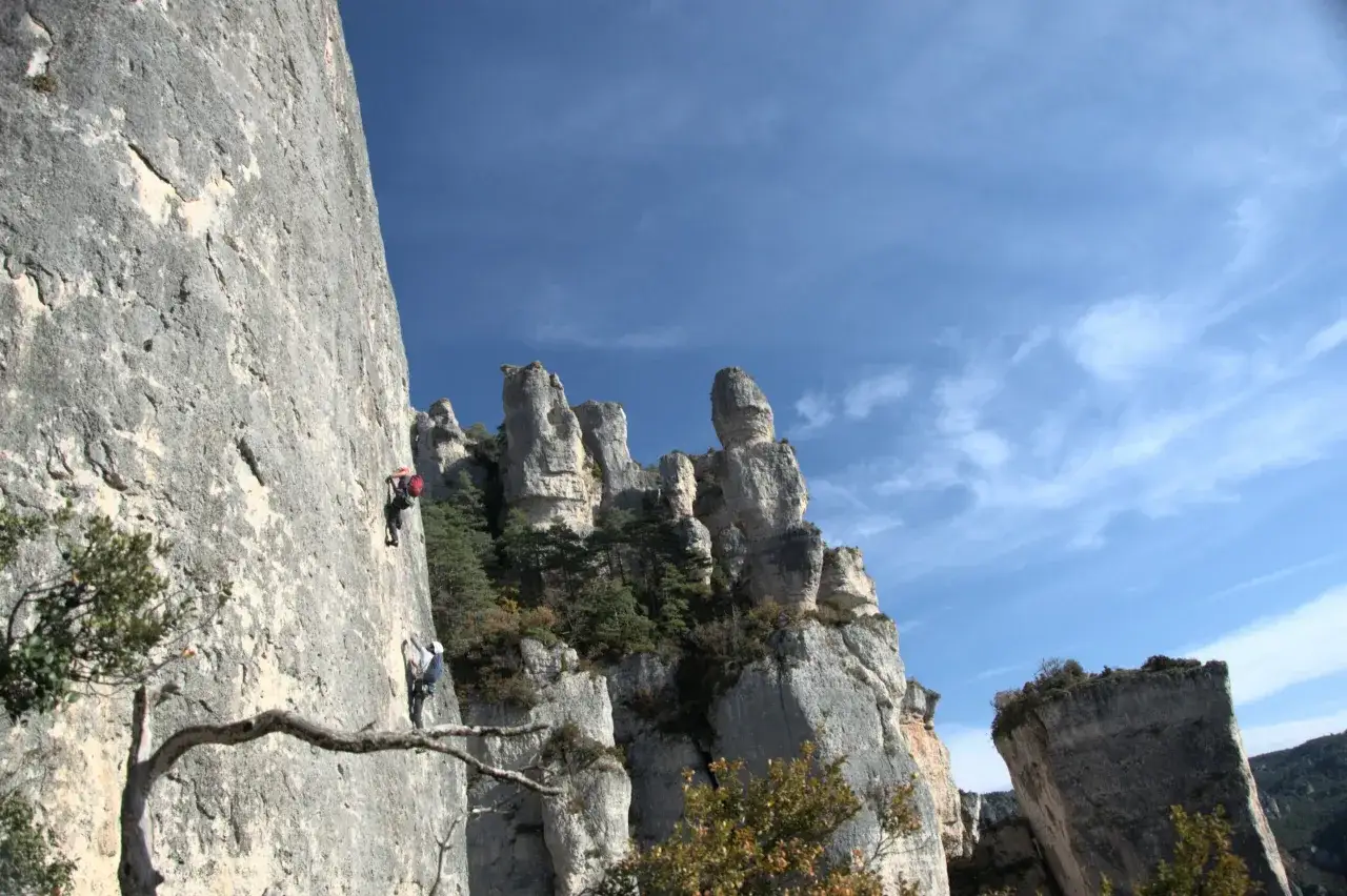 Deux grimpeurs s'élèvent sur une paroi rocheuse abrupte, une scène d'escalade extrême sous un ciel bleu éclatant.