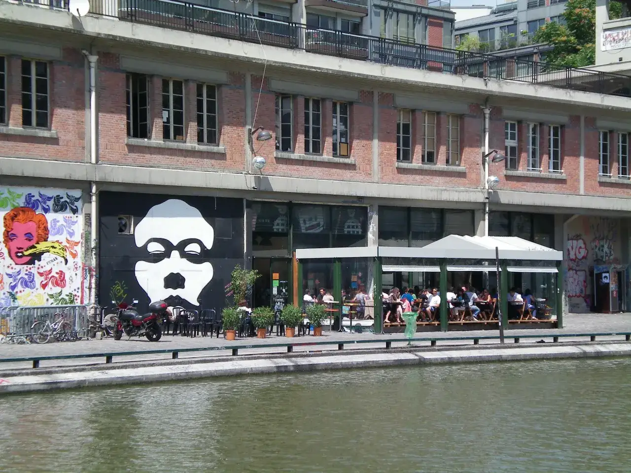 Terrasse animée devant la Paname Brewing Company, avec une grande fresque murale et un canal.