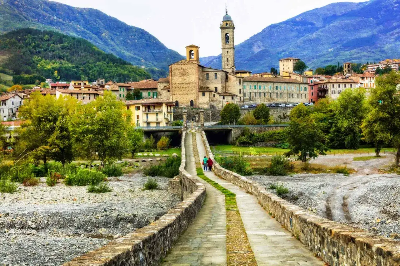 Ponte medievale sul fiume Trebbia, con borgo storico e campanile. Un luogo incantevole da scoprire.